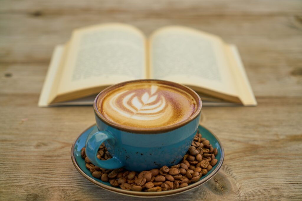 A ceramic cup of latte art coffee on a wooden table with an open book, perfect for relaxation.