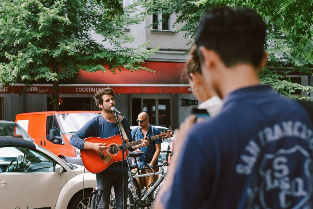 A musician playing guitar and singing outdoors on a city street during the day.